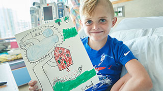 Young boy in a hospital bed holding up a drawing of a house