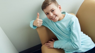 Young boy allergy patient sitting in chair with thump up