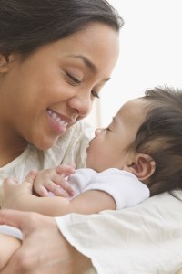 Close up of mother smiling and looking down at a baby sleeping in her arms