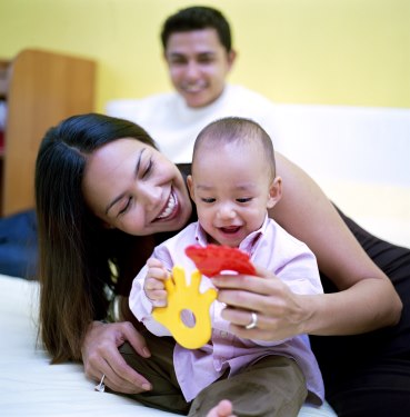 Mother and father with their baby on the bed, playing with objects