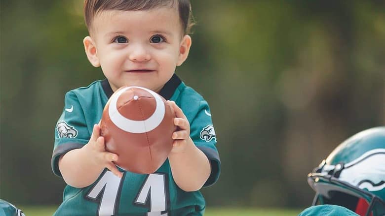 Toddler smiling holding a football, wearing a Philadelphia Eagles jersey
