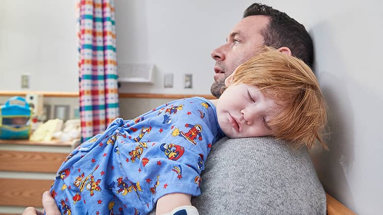 Child asleep on fathers shoulder in exam room