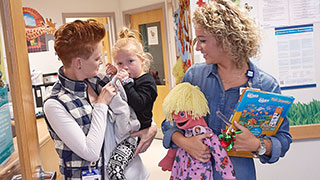 Mom holding Piper as she leaves the phlebotomy lab with a child life specialist