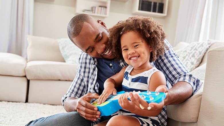 Father helping young daughter play ukulele