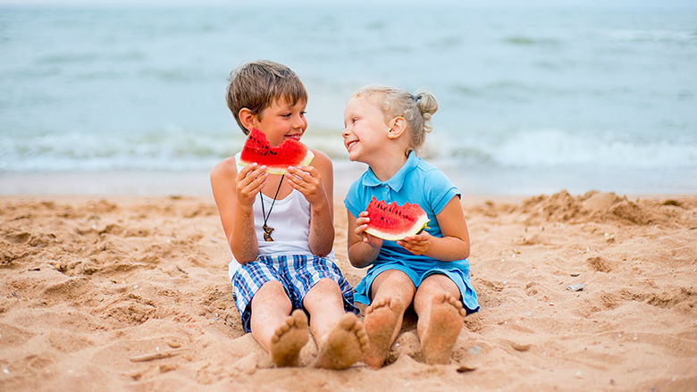 Two kids on the beach eating watermelon