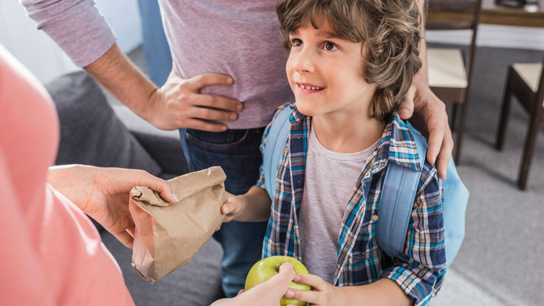 Boy receiving lunch and an apple from parent