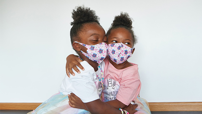 Two young girls wearing protective masks and hugging