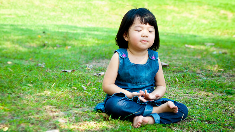 Young girl sitting in the grass, practicing breathing