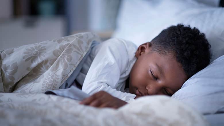 Child tucked into bed with white covers