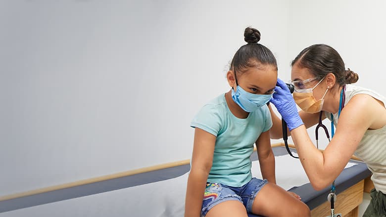 Doctor looking in patients ear, both wearing PPE