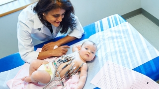 Doctor observing baby with ECG leads connected