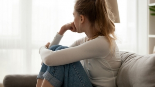 young depressed teen siting in couch looking out window