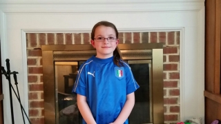 Emma wearing a soccer jersey smiling standing in front of a fireplace