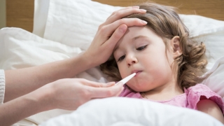 young girl sick in bed with thermometer in mouth