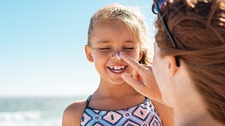 Girl smiling getting sunscreen put on her nose.