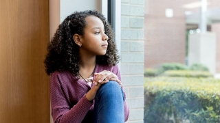 Adolescent girl sadly looking out window