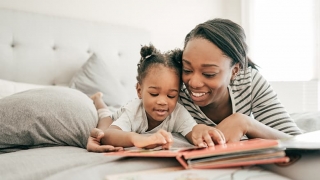 Mother laying on bed reading to daughter