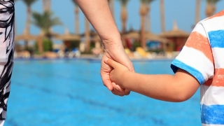 Parent and child holding hands at a pool