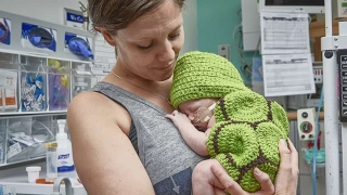 Mom holding in infant in a knitted turtle costume (very cute)