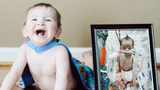 Jaxon smiling next to photo of him in hospital as infant