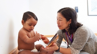 Elena Huang, M.D., a pediatrician at the Nicholas and Athena Karabots Pediatric Care Center, shares a book with Waldis, 8 months, as part of CHOP’s Reach Out and Read program.