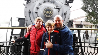 Sam standing outside with his brother and father by a locomotive