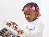 Child with braids and pink floral hair clips reading a book.