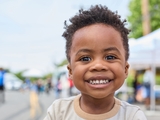 Smiling child with curly hair and beautiful big eyes wearing a beige t-shirt.