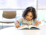 Toddler reading a book at a table.