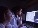 People in white coats looking at a computer screen in dark room.