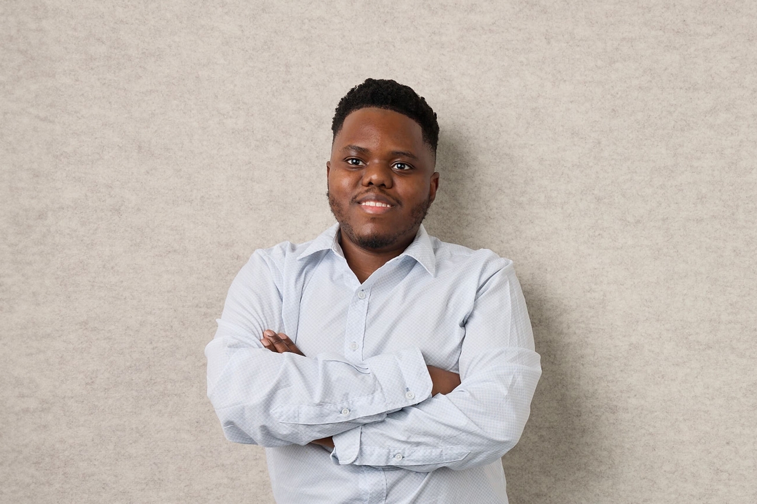 Smiling confident young man with arms folded in front of cream wall