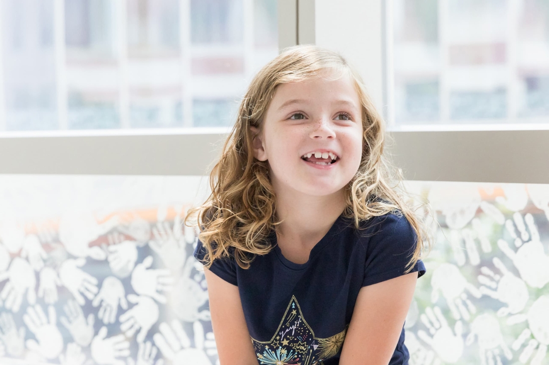 Blonde freckled girl sitting by the window and smiling