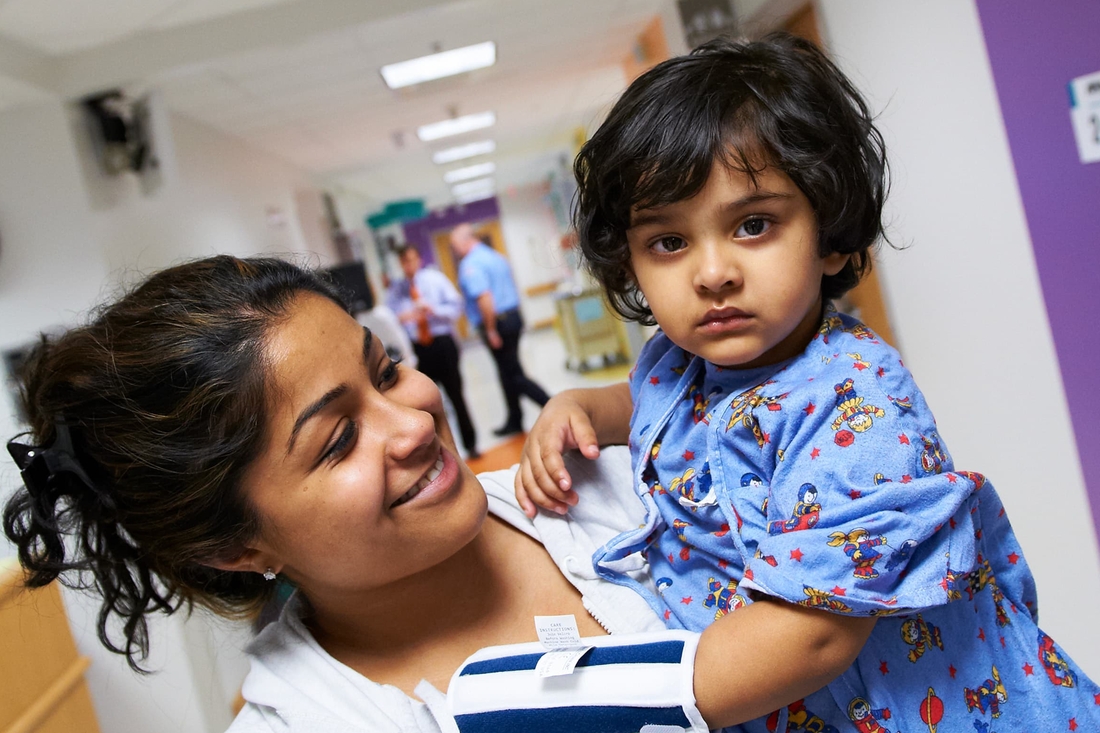 Mommy holding her little trooper in a busy hospital hallway