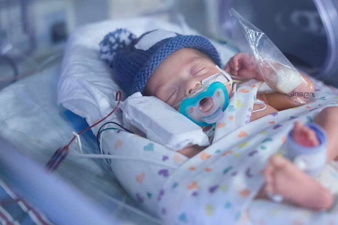 Premature baby with blue hat sleeping in an incubator
