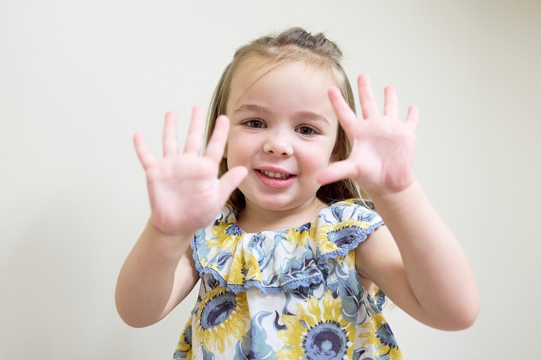 Blonde girl wearing a sunflower dress with her palms close to her face.