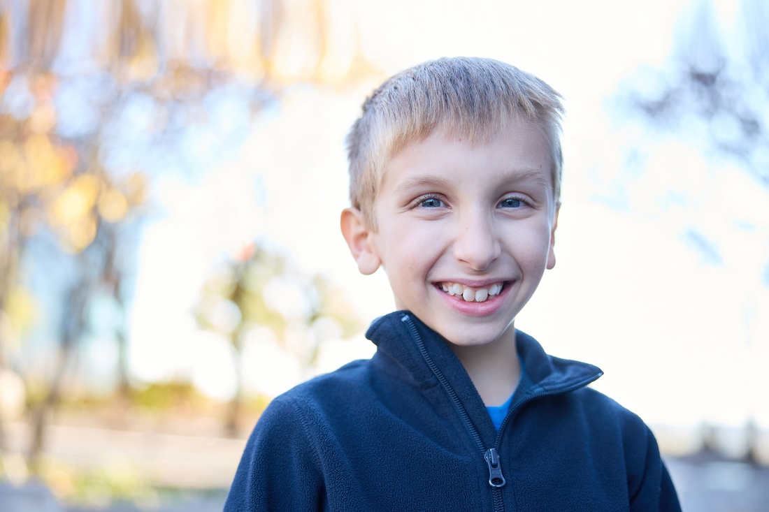 Smiling blonde boy with blue eyes wearing a dark blue jacket.