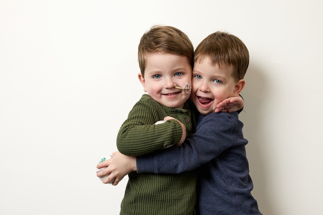 Twin brothers with blue eyes hugging each other.