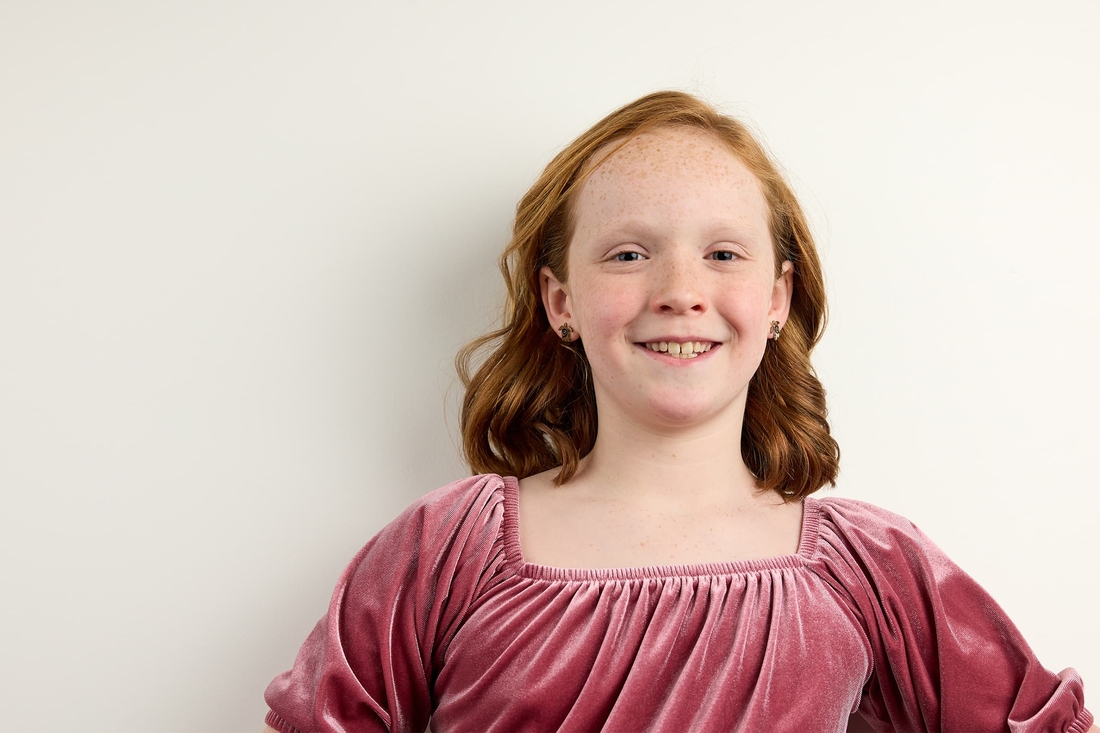 Smiling redhead girl wearing a pink velvet blouse.