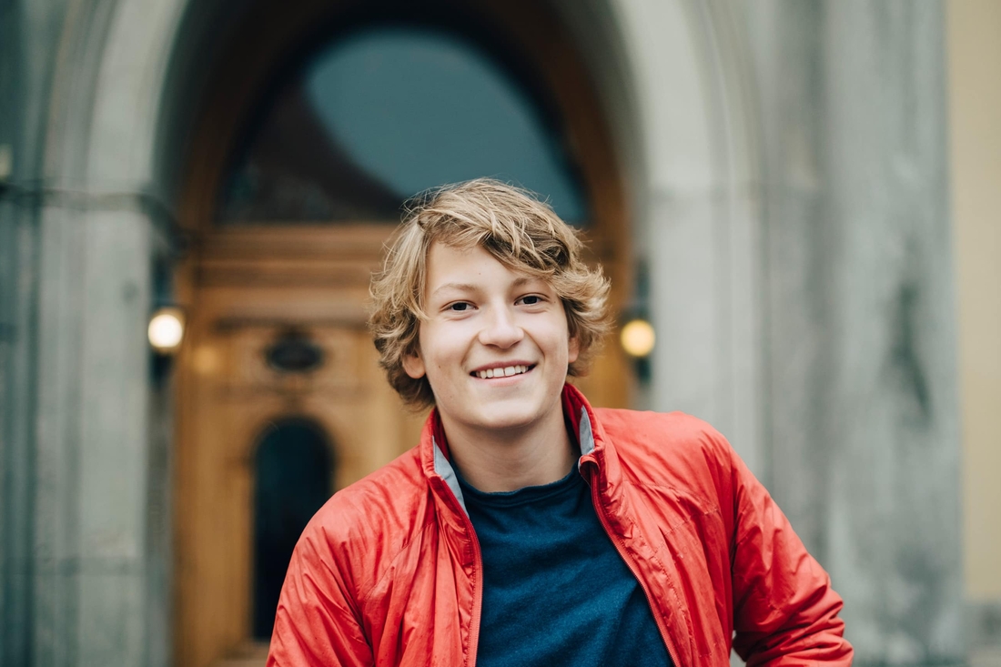 teen standing in front of a stone building wearing a red jacket