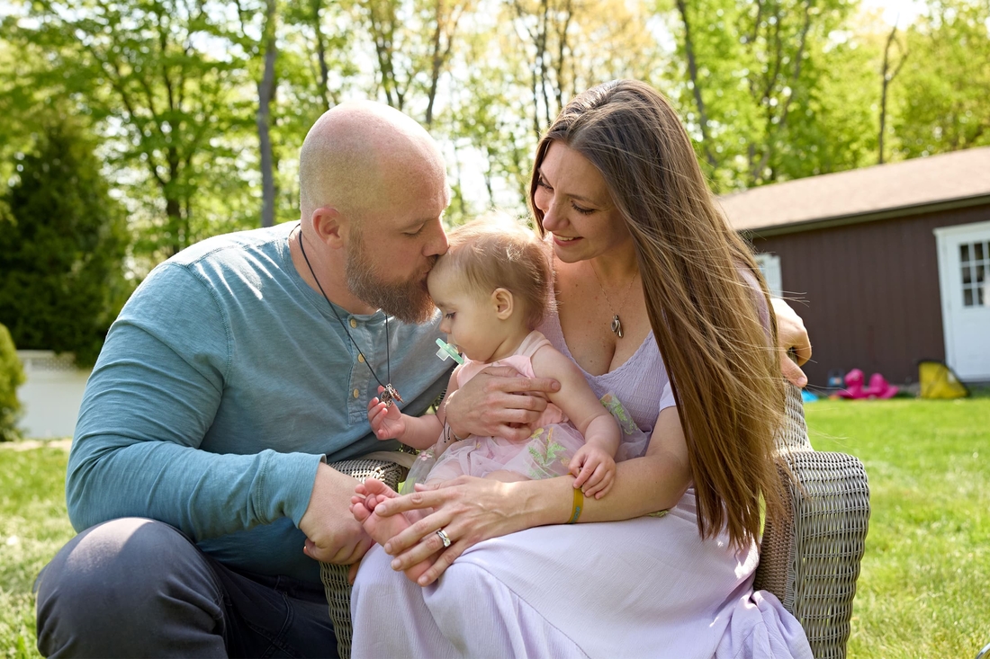Beautiful family outside with Father, Mother, and baby looking at necklace containing ashes of her sister.