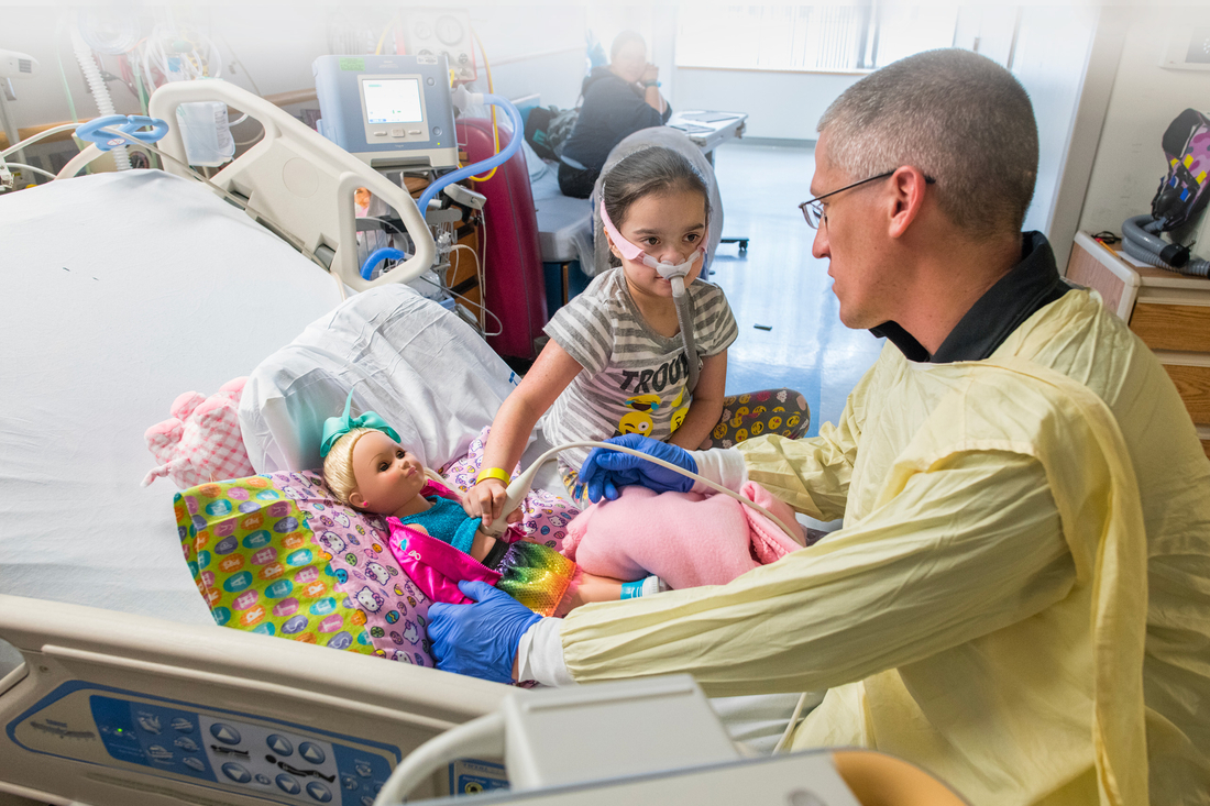 Nursing staff sits with a child as she learns how to do an ultrasound on her babydoll