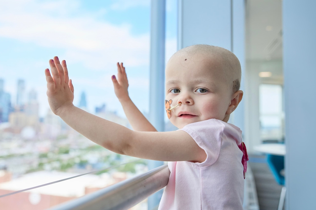 Little girl bald with cancer looks hopeful and happy at viewer.