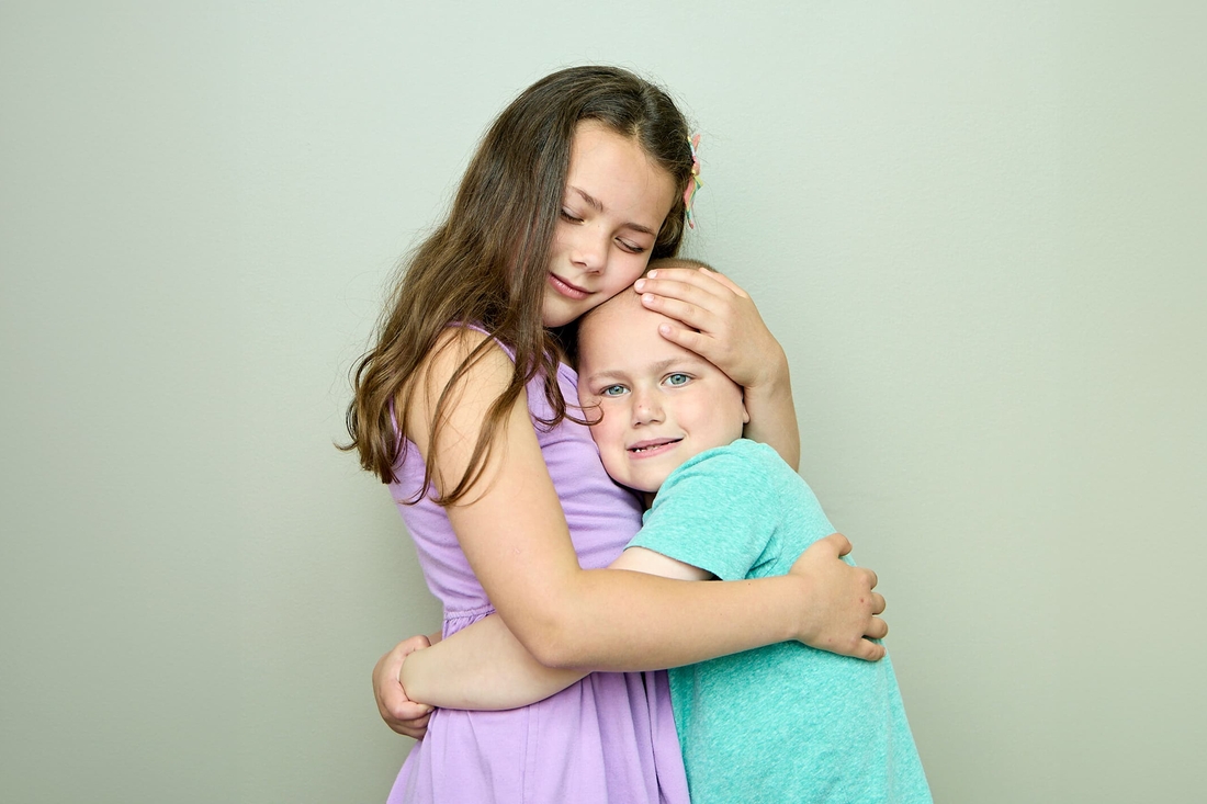 Older sister in purple dress hugging and offering support to her younger sister who is a cancer survivor.