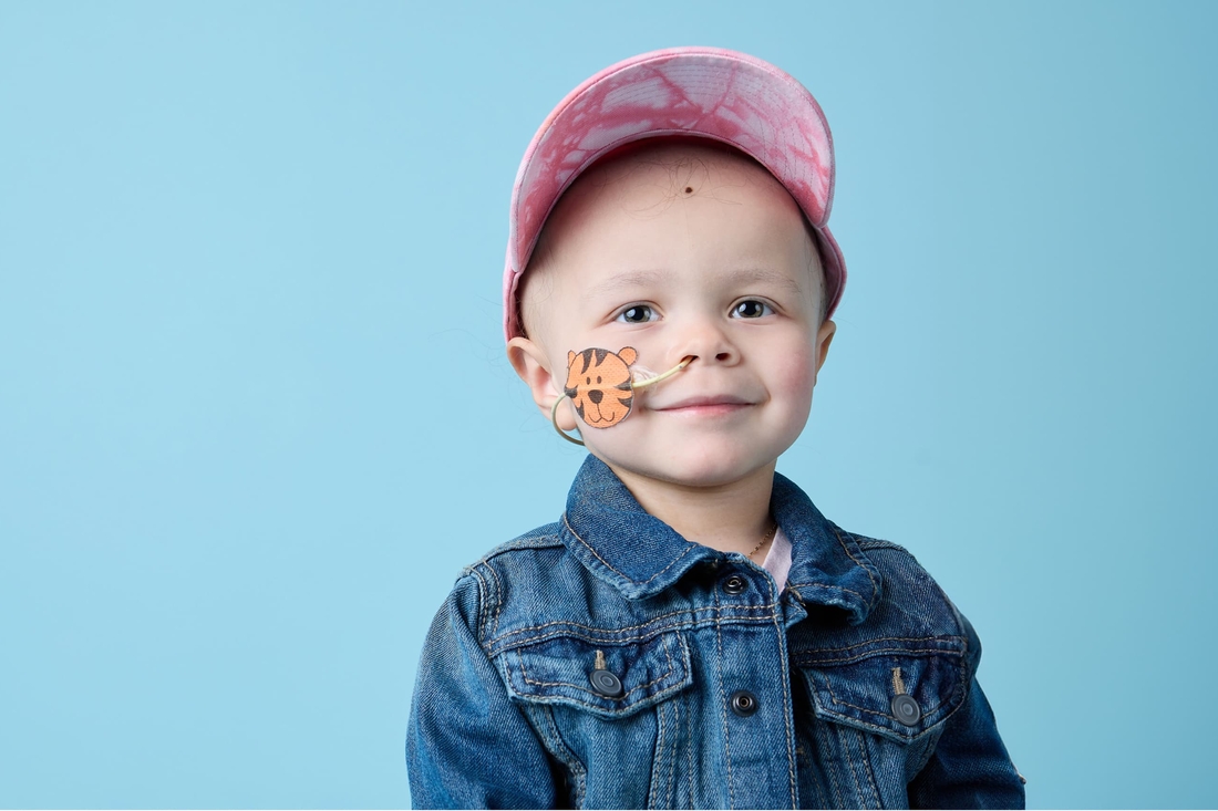 Adorable young child cancer survivor with air tube in nose wearing a cap.