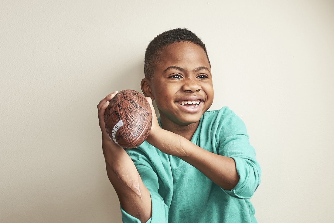 boy with transplanted hands holding a signed American football.