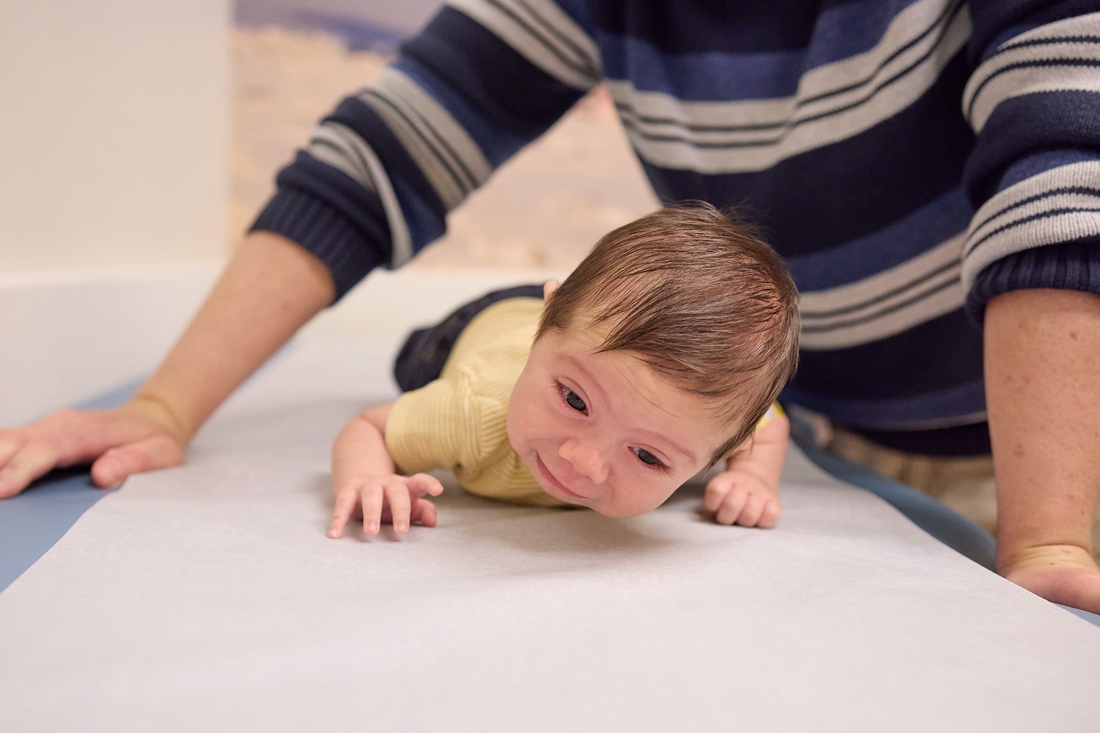 Infant boy on exam table attempting to crawl and doctor is above him.