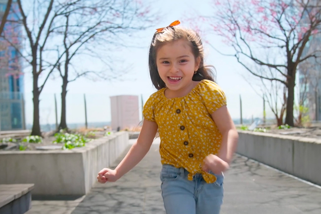 Smiling girl running outside towards the camera with a reconstructed ear.