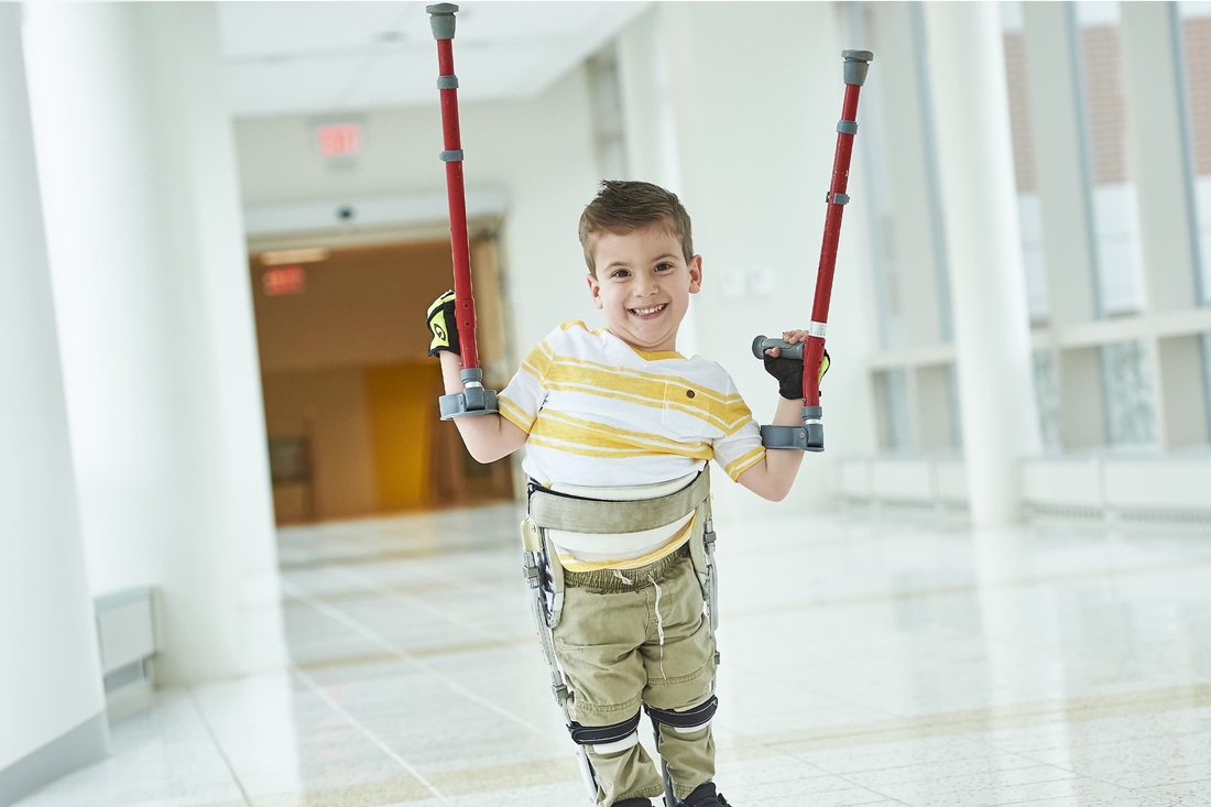 Boy smiling holding up his crutches wearing stiped tshirt.
