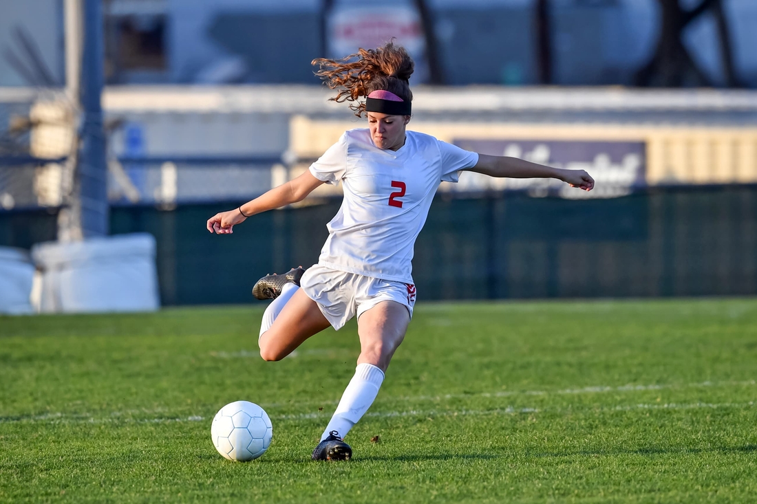 Older teen girl playing soocer and kicking the ball hard showing hip movement.