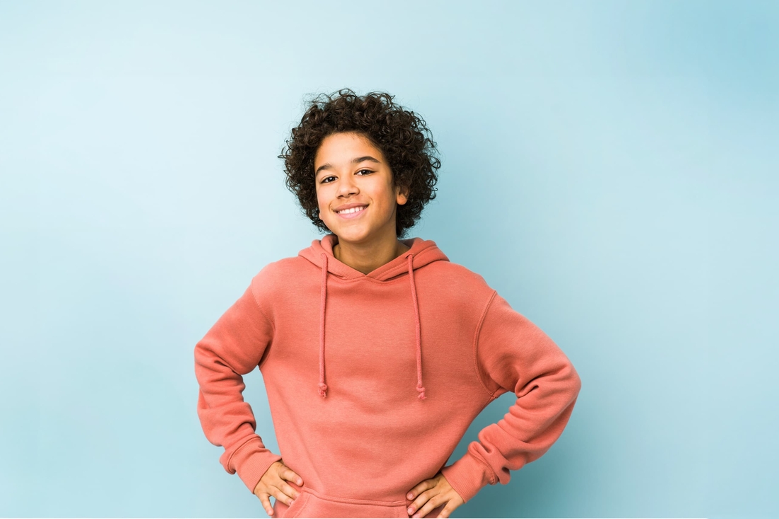 Teenager smiling with hands on their hips, wearing a coral sweatshirt.
